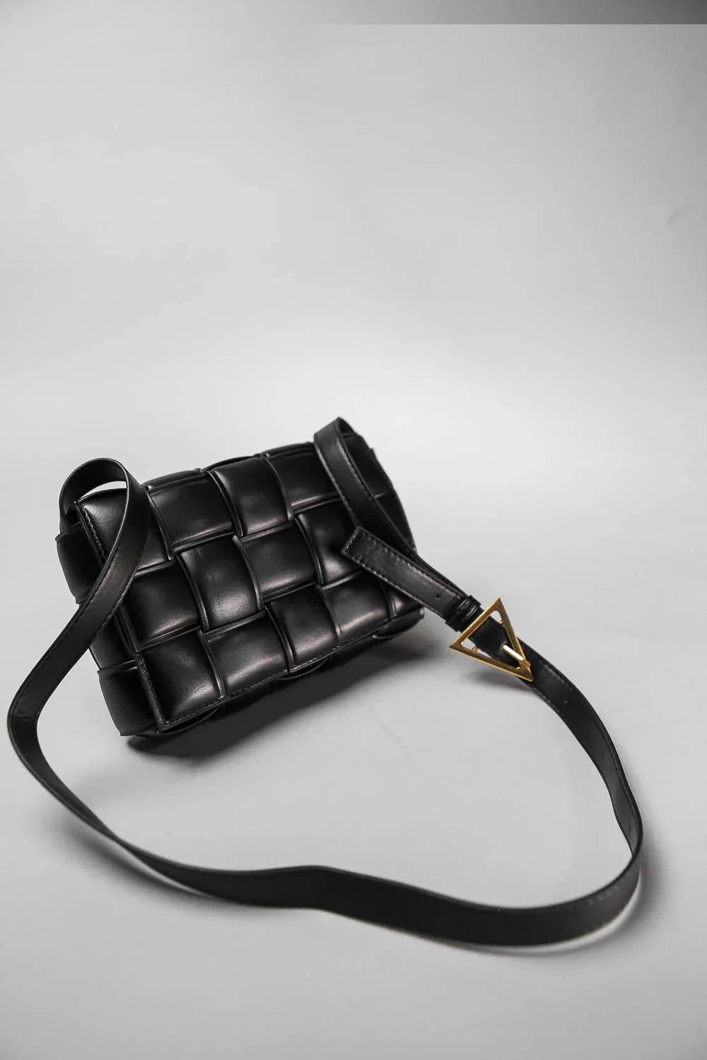 Black woven handbag with a gold clasp on a light gray background