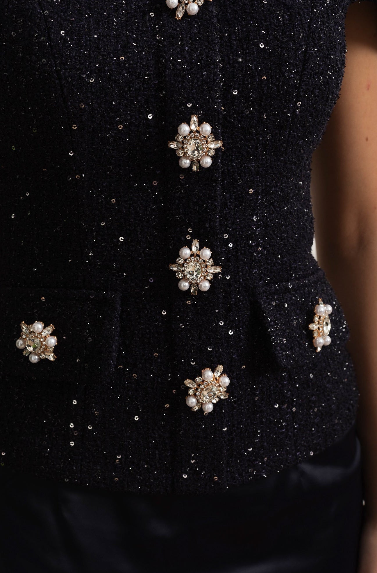 Black textured fabric with decorative buttons featuring pearls and crystals.