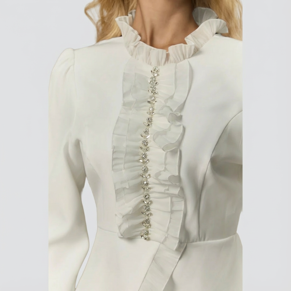 Close-up of a white blouse with ruffled details and a decorative trim on a light gray background