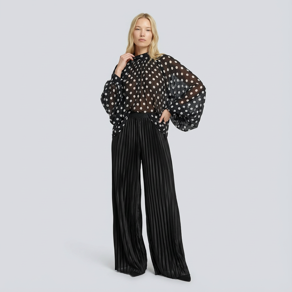Woman wearing a black polka dot blouse and black pleated pants on a light gray background