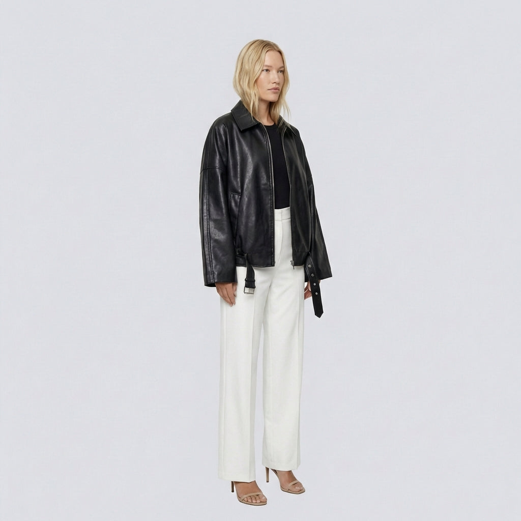 Woman wearing a black leather jacket and white pants on a light gray background