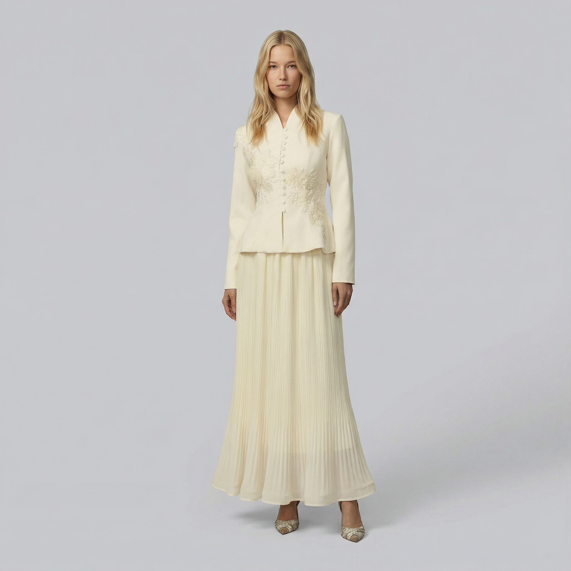 Woman wearing a cream-colored suit with a jacket and pleated skirt on a plain background