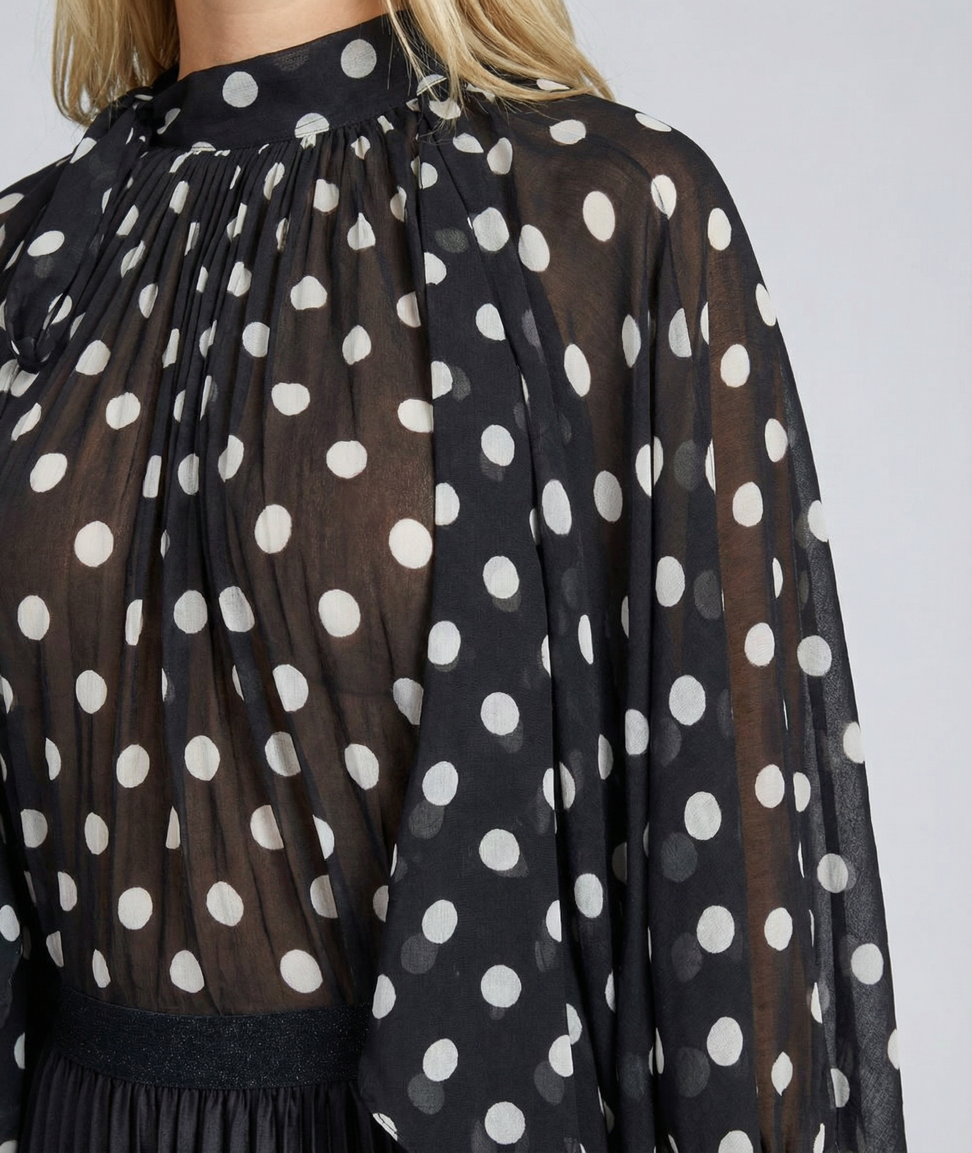 Black blouse with white polka dots on a plain background
